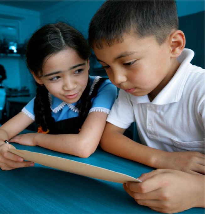 A boy and a girl sitting in a classroom and reading together