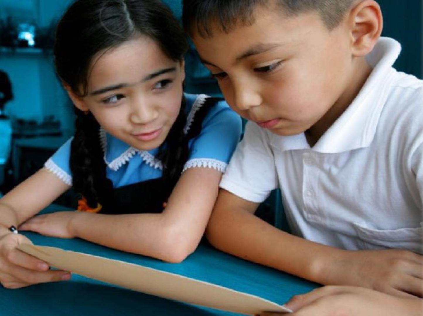 A boy and a girl sitting in a classroom and reading together